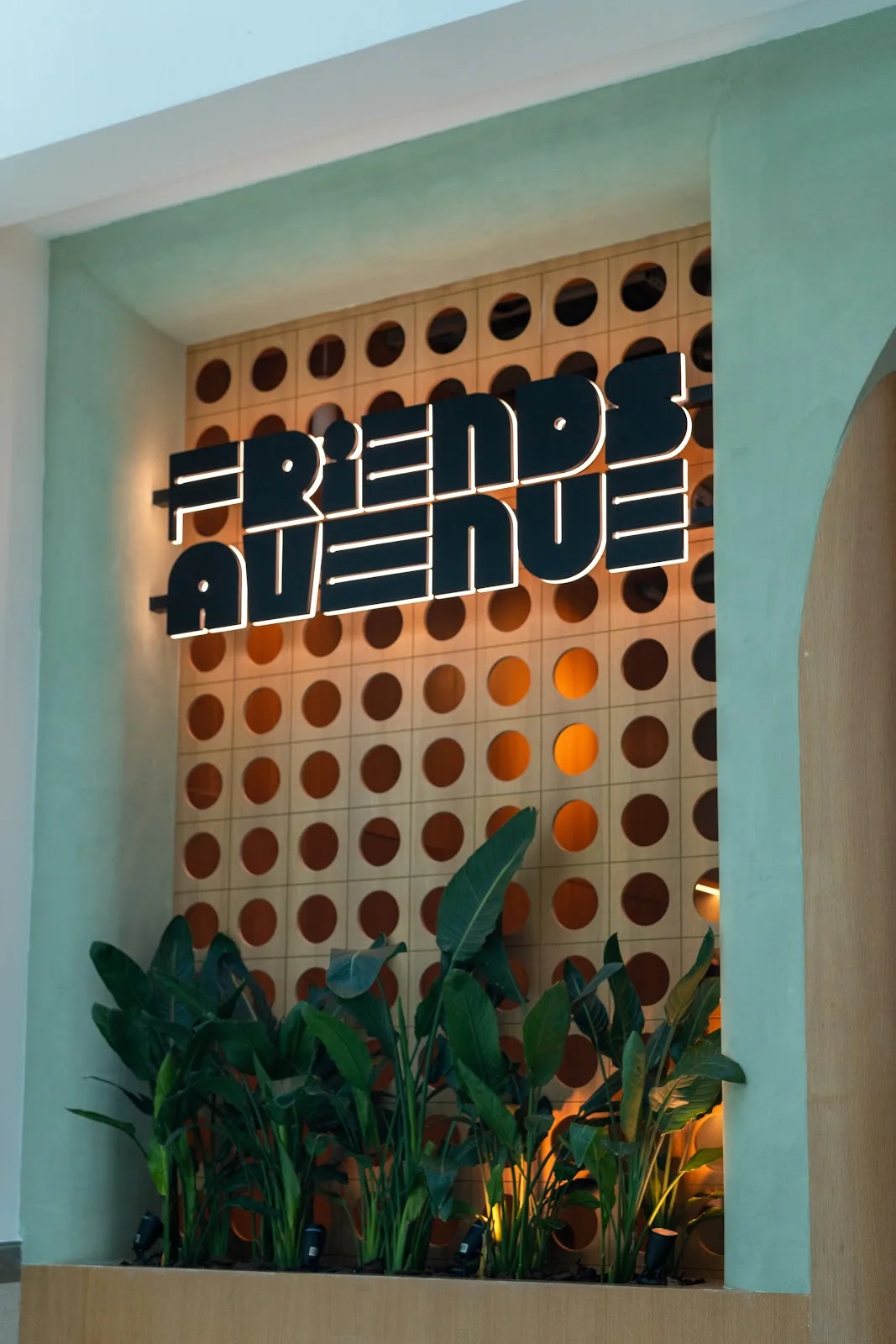 Illuminated Friends Avenue signage on a terracotta perforated wall framed by tropical plants