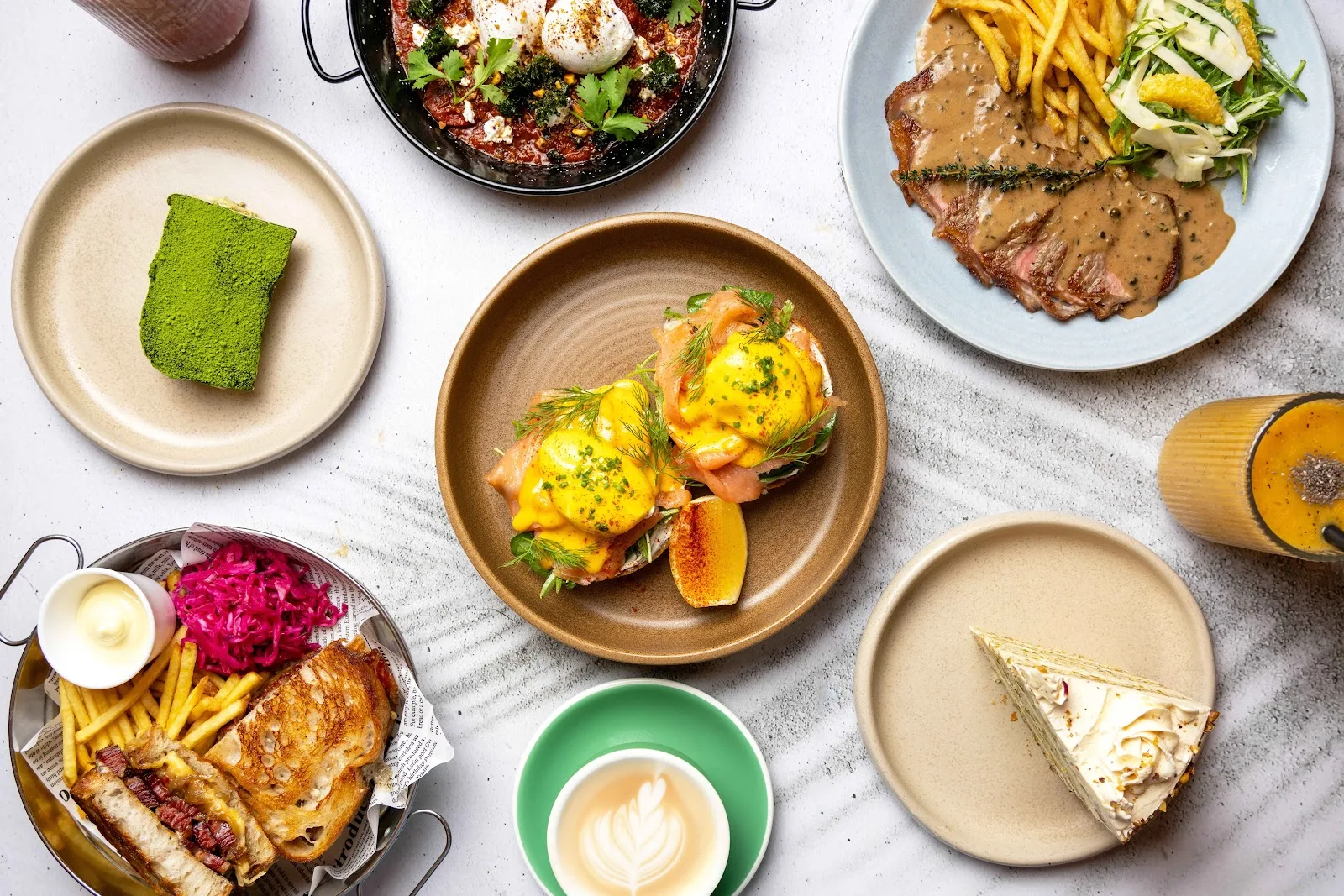 A spread of brunch dishes, eggs benedict, cake and coffee on a marble table