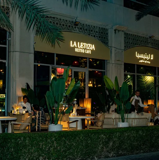 La Letizia café and shisha lounge storefront glowing at night on Dubai Marina Walk, framed by tropical greenery