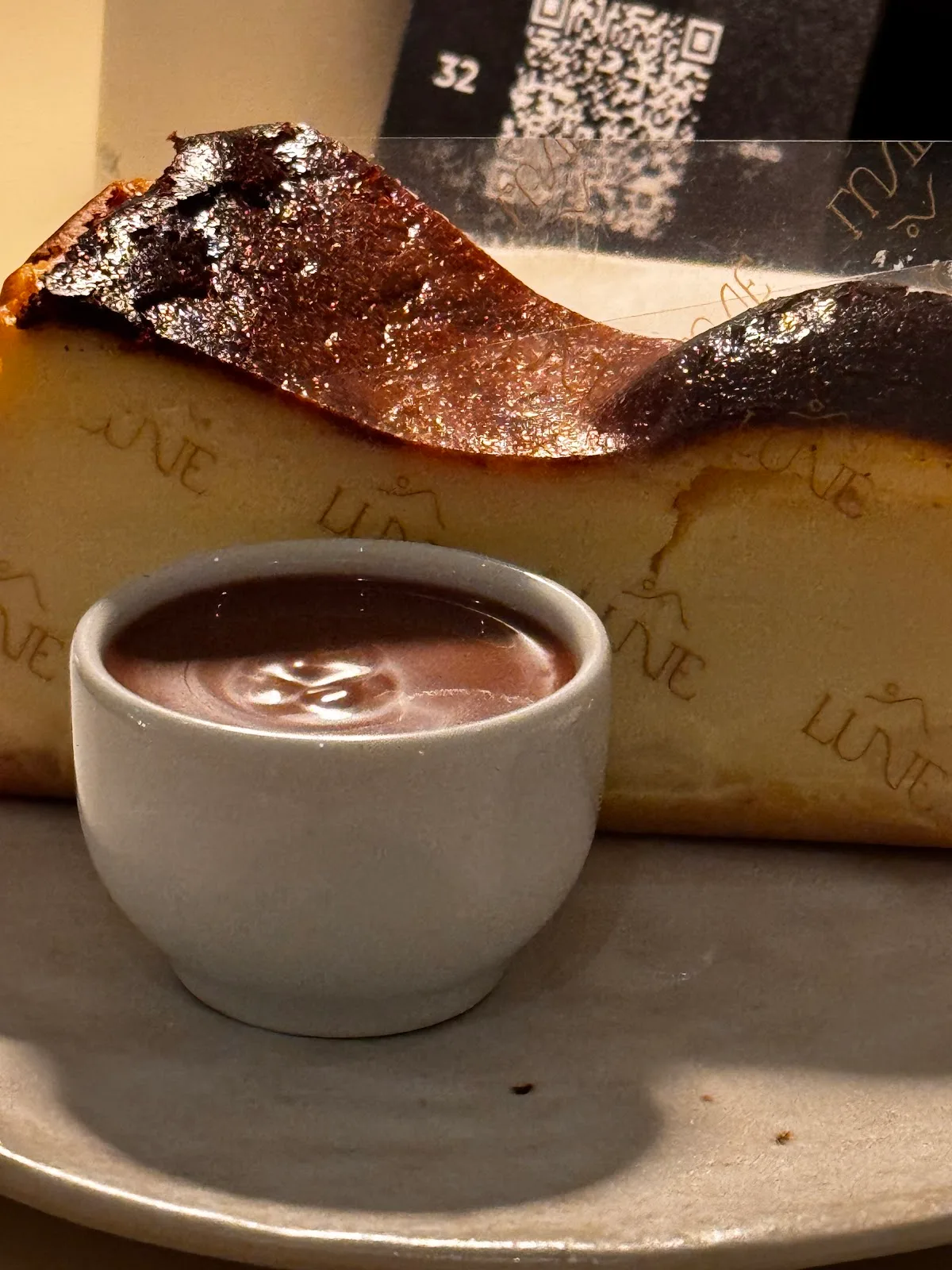 A burnt Basque cheesecake branded with the Lune name, served with a cup of hot chocolate.