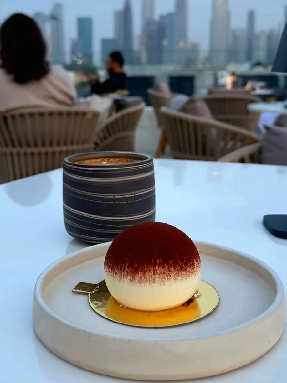 A plated dessert and coffee on the rooftop with skyline behind.