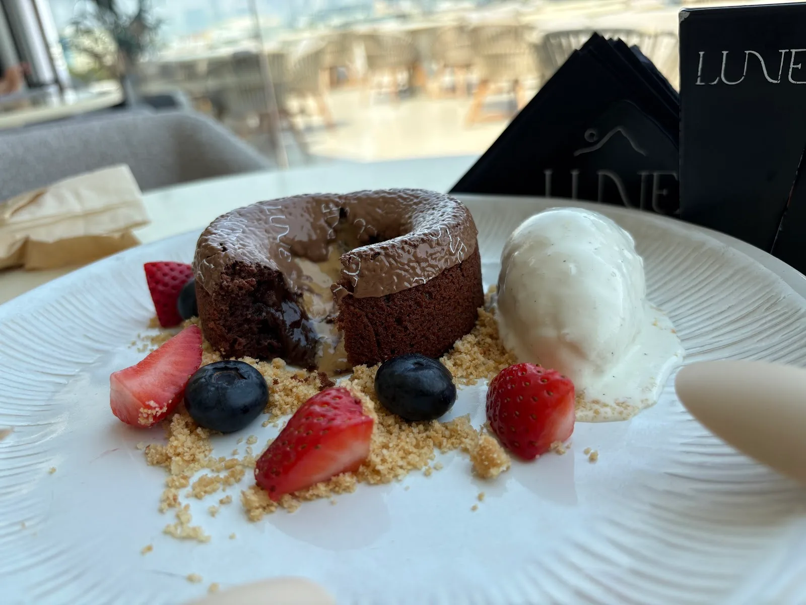 A molten chocolate lava cake branded Lune, cut open beside vanilla ice cream and berries.