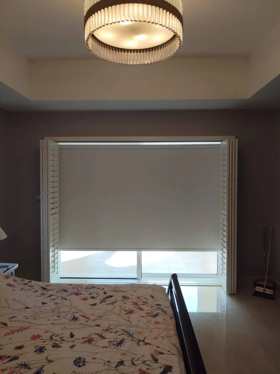 Blackout roller blind fitted behind plantation shutters in a bedroom