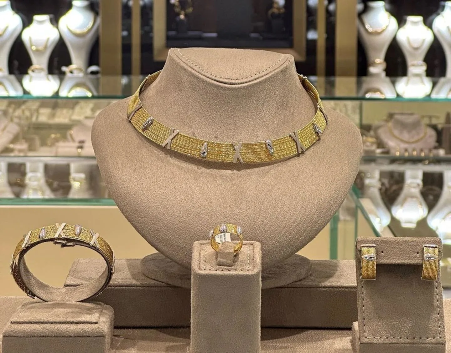 A matching gold necklace, bracelet, ring and earrings displayed on suede busts at Hadeed Jewellery