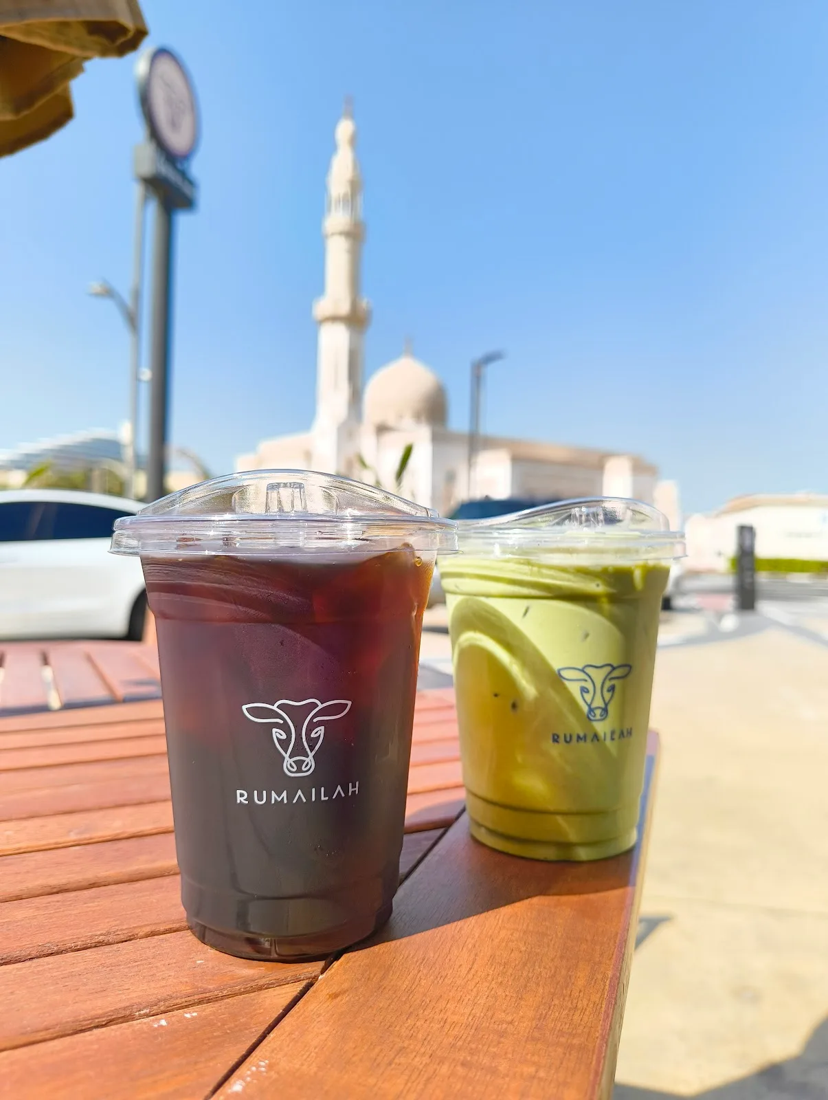 Iced coffee and matcha latte in Rumailah cups on an outdoor table with the Jumeirah mosque behind