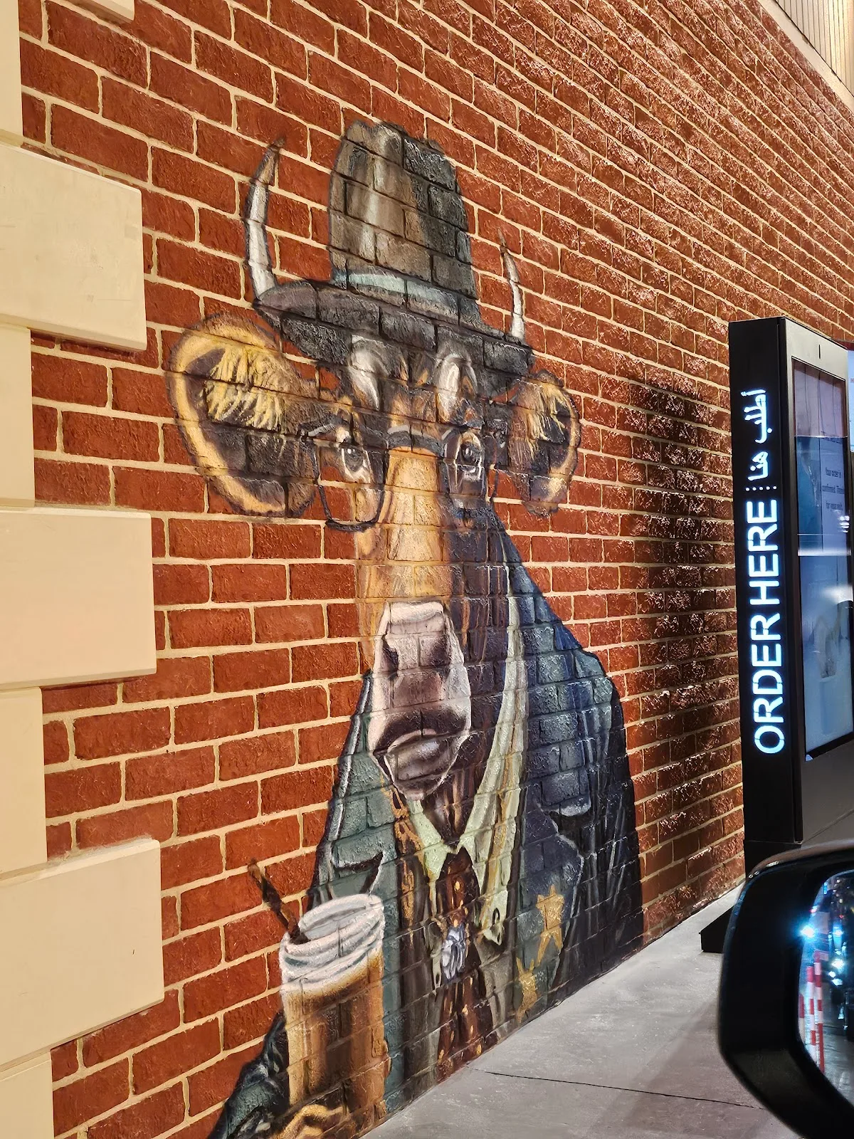 Hand-painted mural of a cow in glasses holding an iced coffee