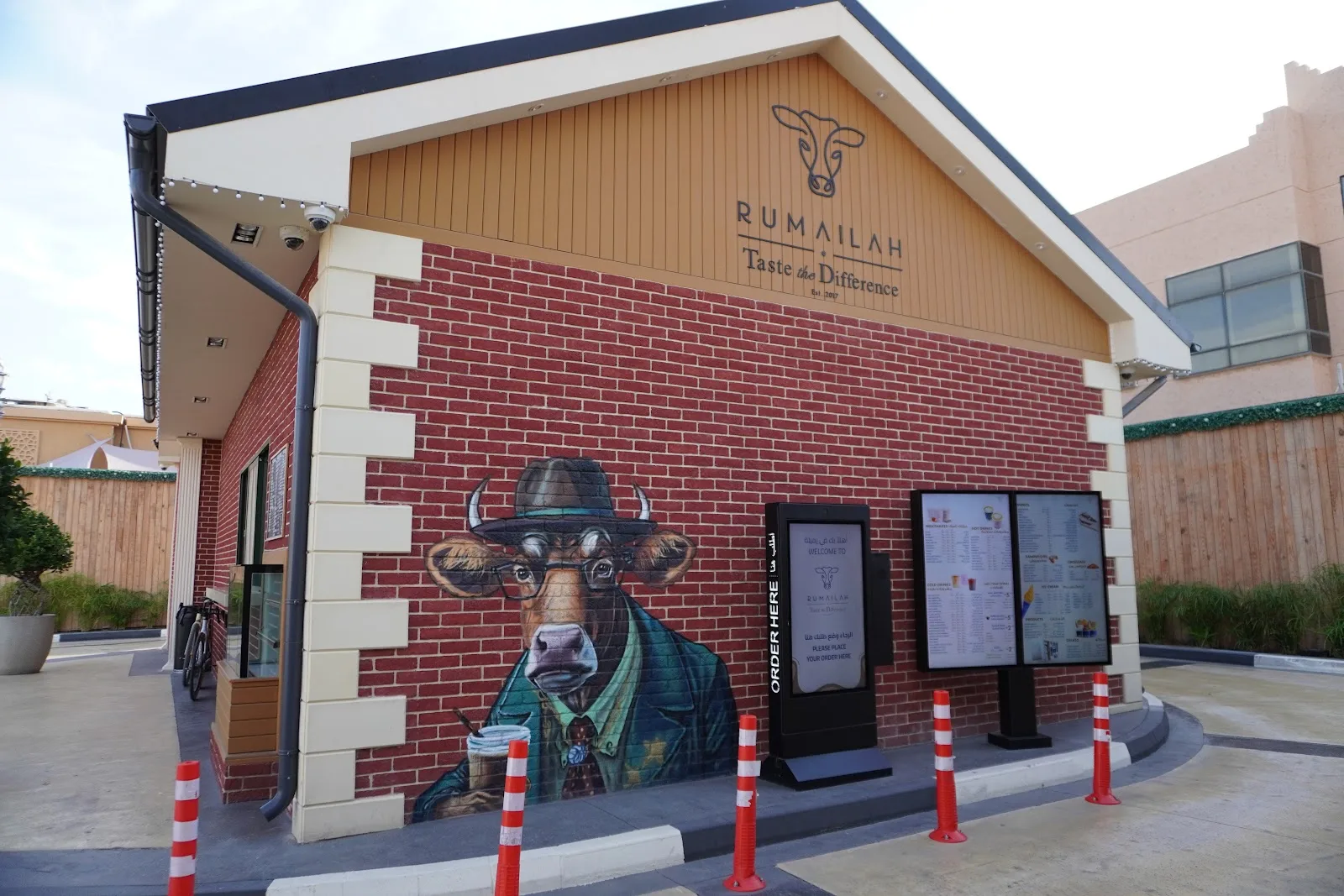 Rumailah Café storefront — red brick with a hand-painted mural of a cow in a hat and the Taste the Difference sign