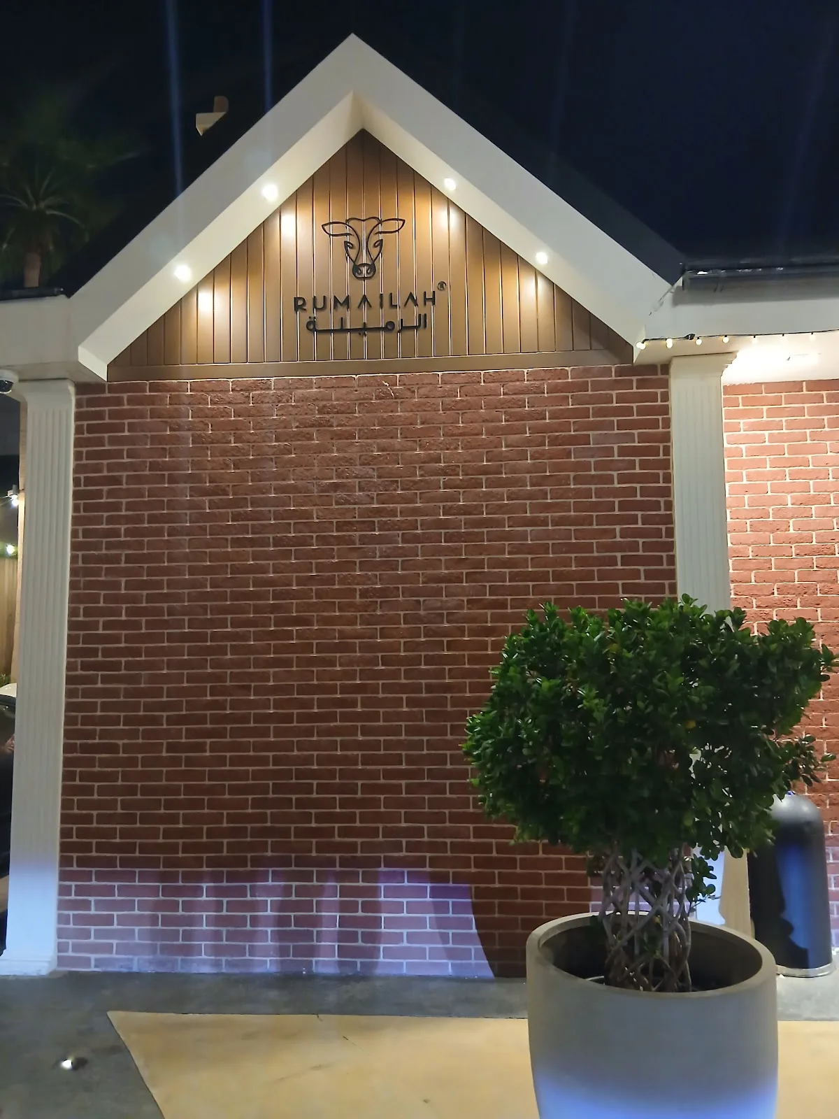 Rumailah café entrance at night with brick gable and greenery
