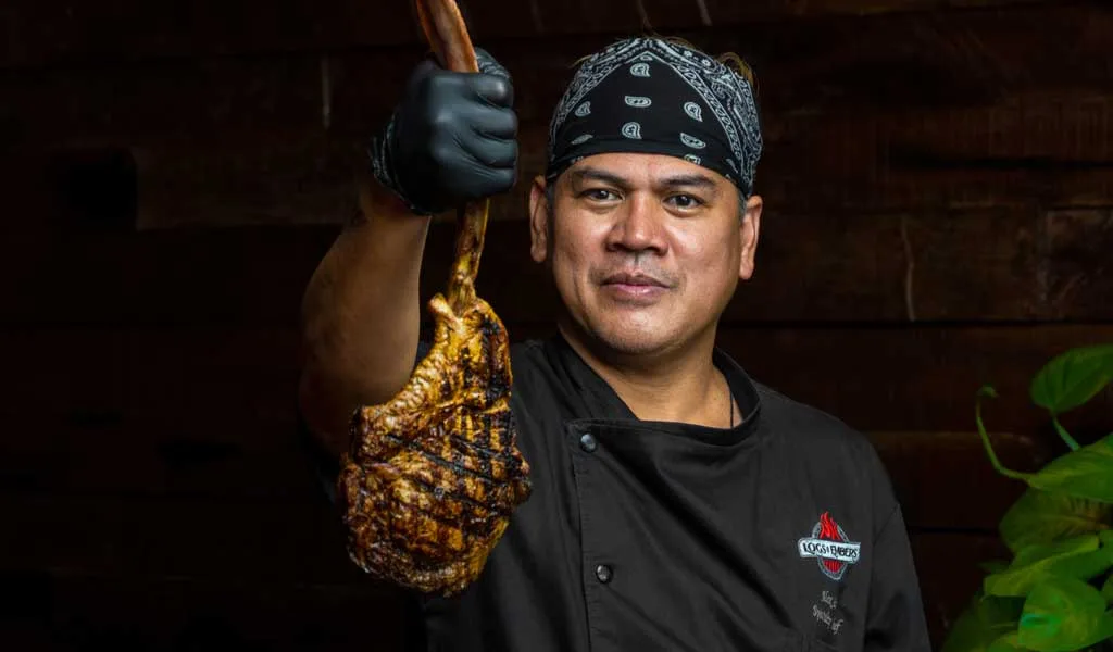Chef presenting a fire-grilled steak in smoke at Logs & Embers