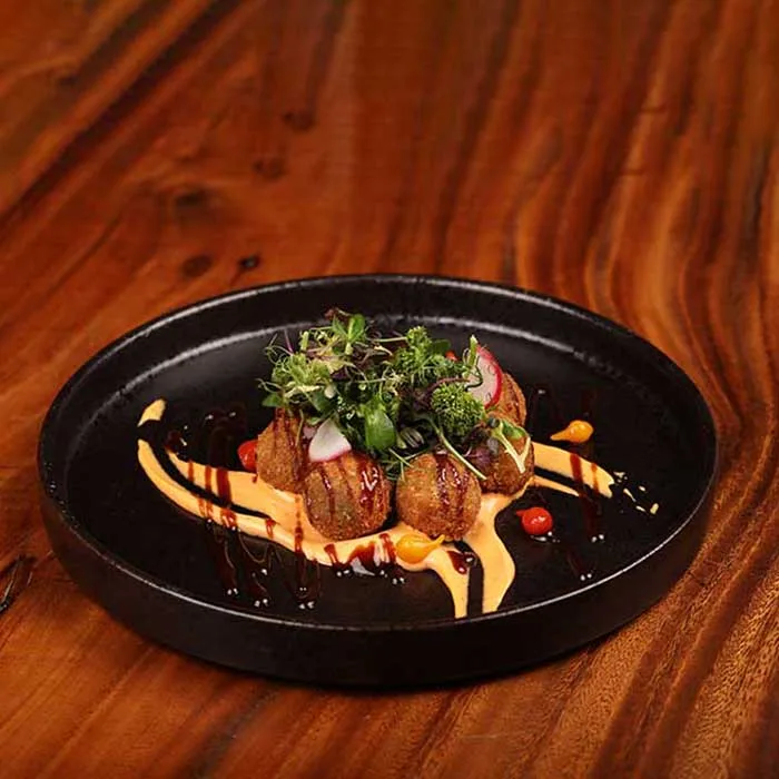Golden croquettes plated with smoked aioli and fresh leaves