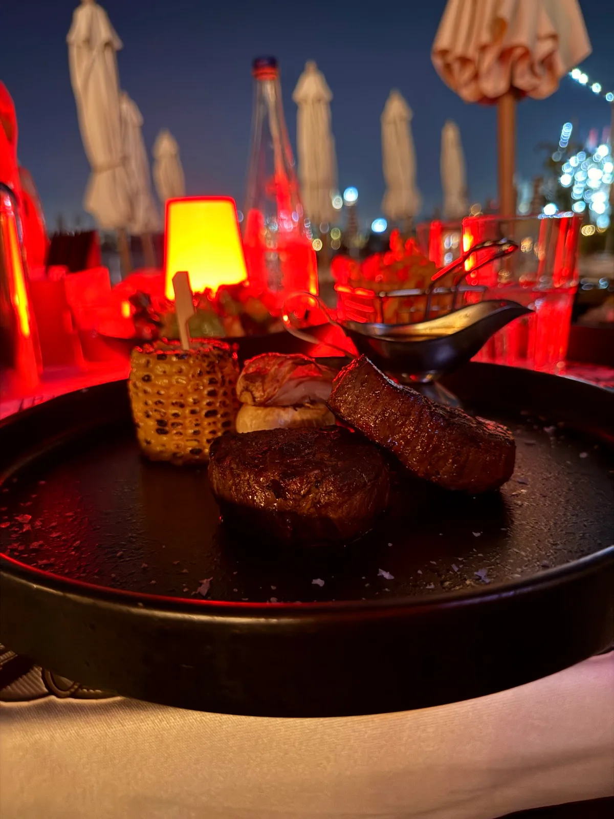 Fire-grilled steak with charred corn and fries, served at dusk by the beach