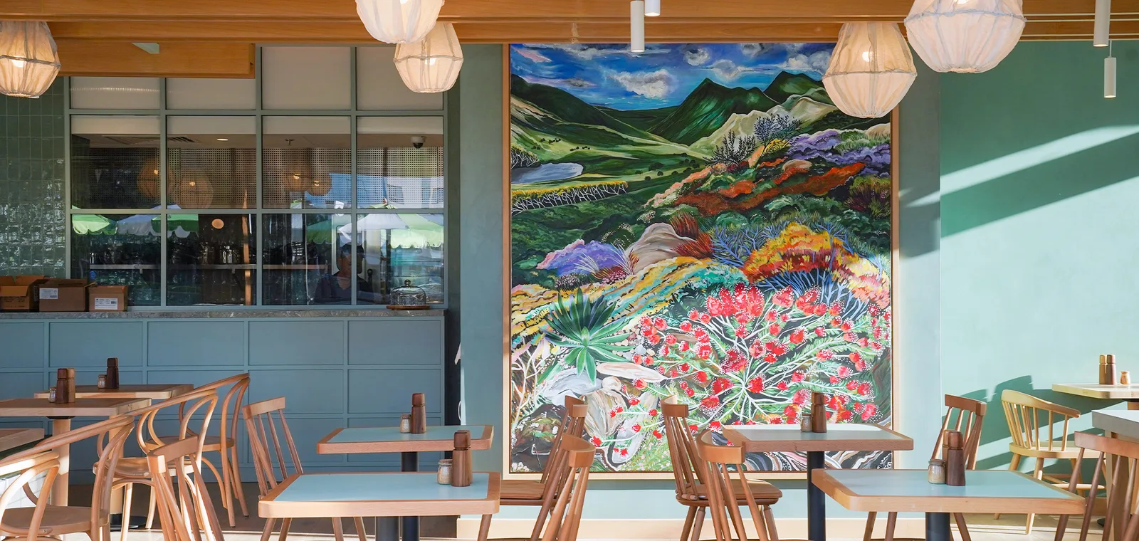 Dining room with sage-green walls, warm wood furniture and a large hand-painted landscape mural