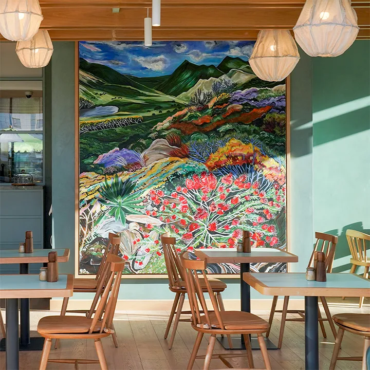 Hand-painted landscape mural behind wooden cafe tables