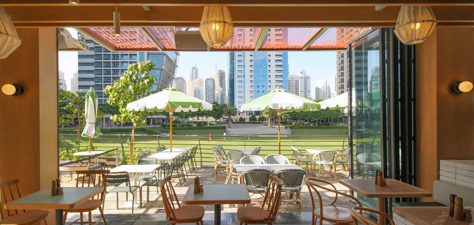 Splendour Fields terrace looking onto The Park lawn with green parasols and the JLT skyline beyond