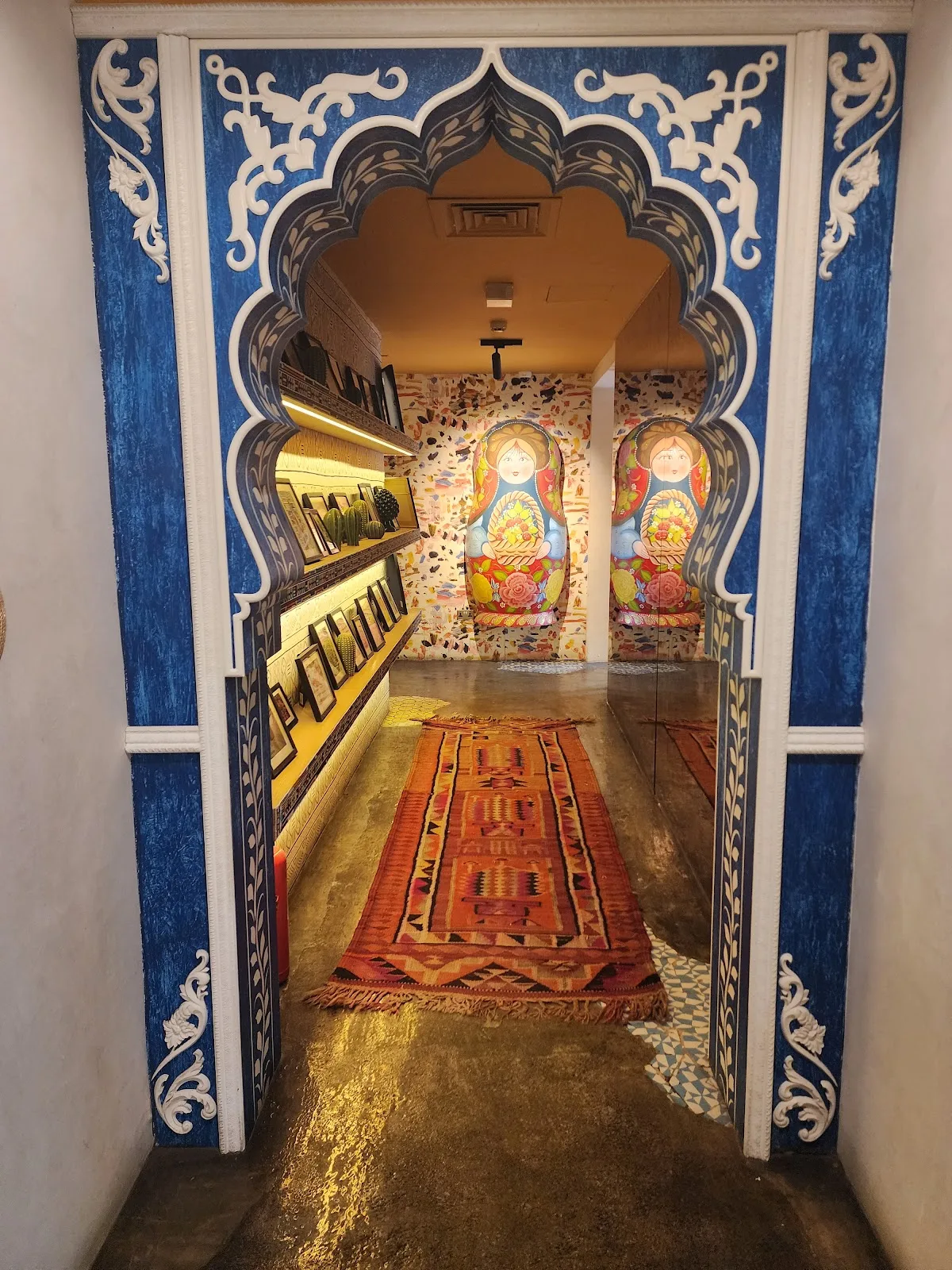 A hand-painted blue Mughal-style arch framing a hallway with murals and a kilim runner.