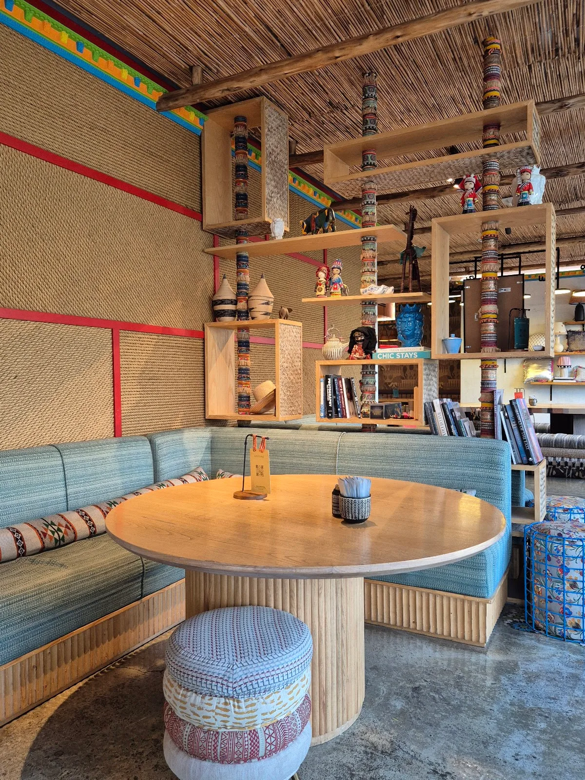 Woven walls and timber shelves filled with global crafts above a teal banquette.