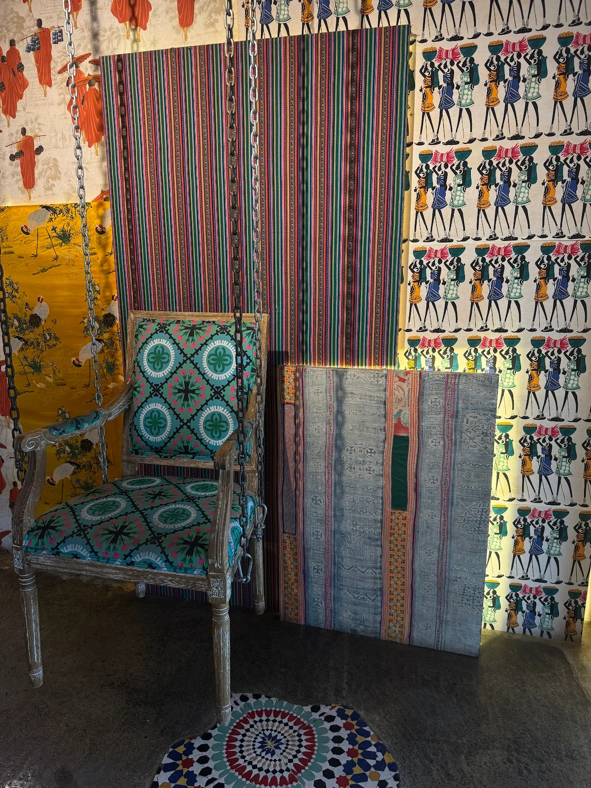 A corner of the pop-up layered with patterned fabrics, a carved chair and a tiled rug.