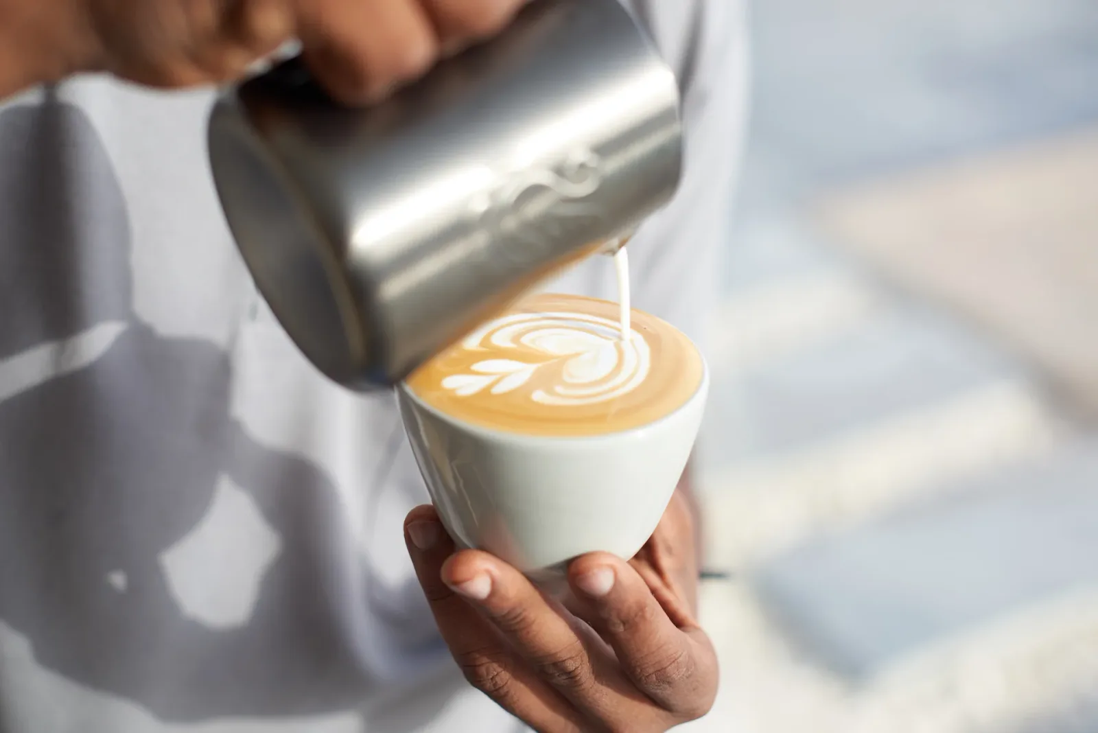 Barista pouring latte art into a flat white at Alchemy Coffee