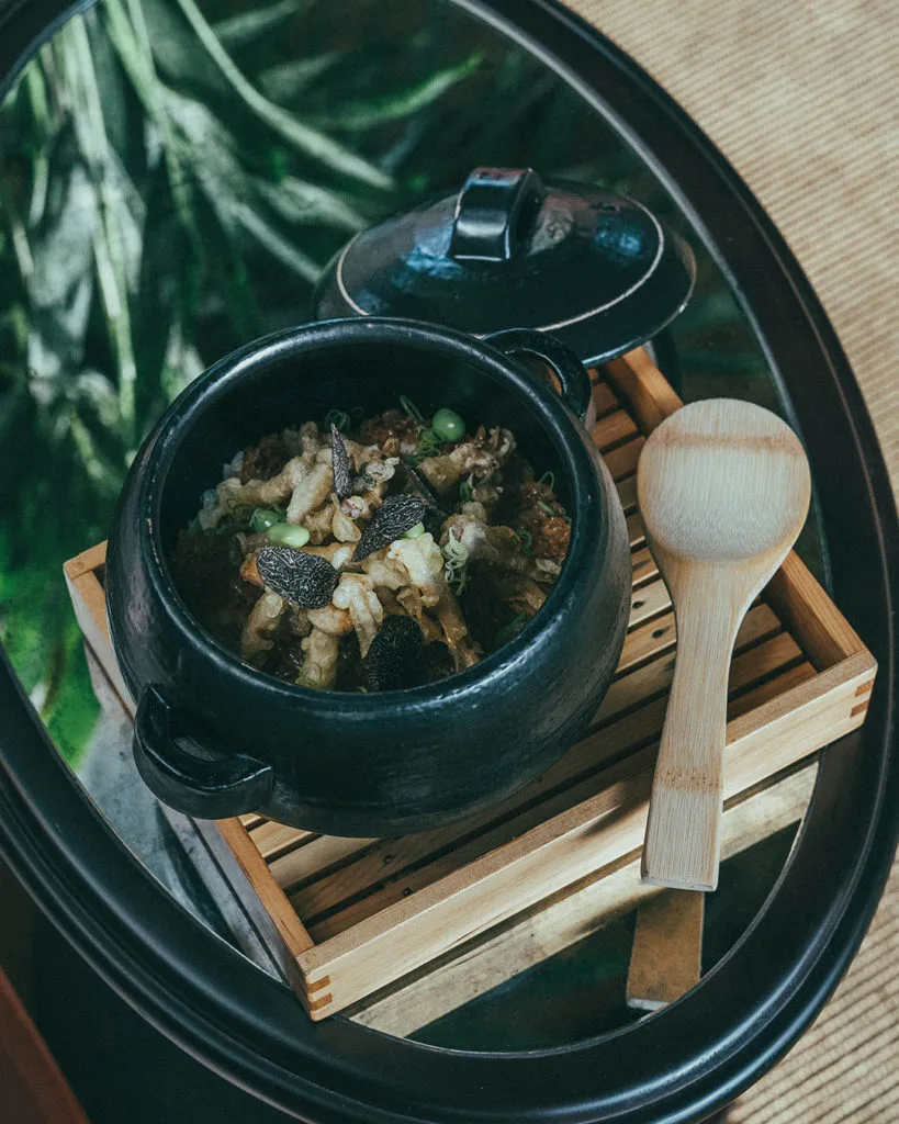 Clay-pot rice served on a bamboo stand with a wooden spoon