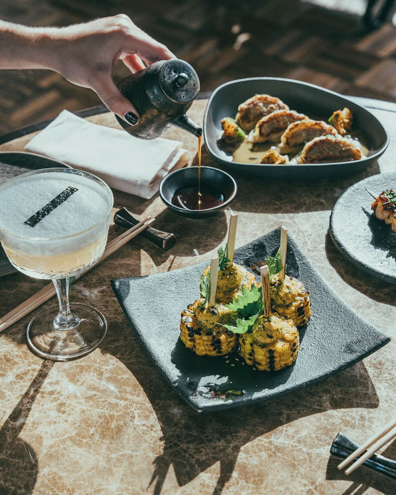 Grilled skewers and corn with sauce being poured