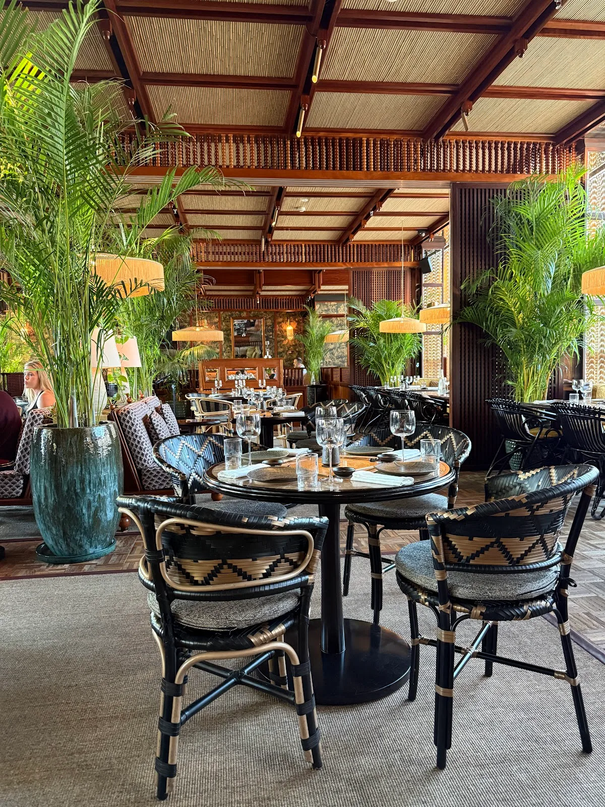 The main dining room with palms, rattan chairs and woven ceiling