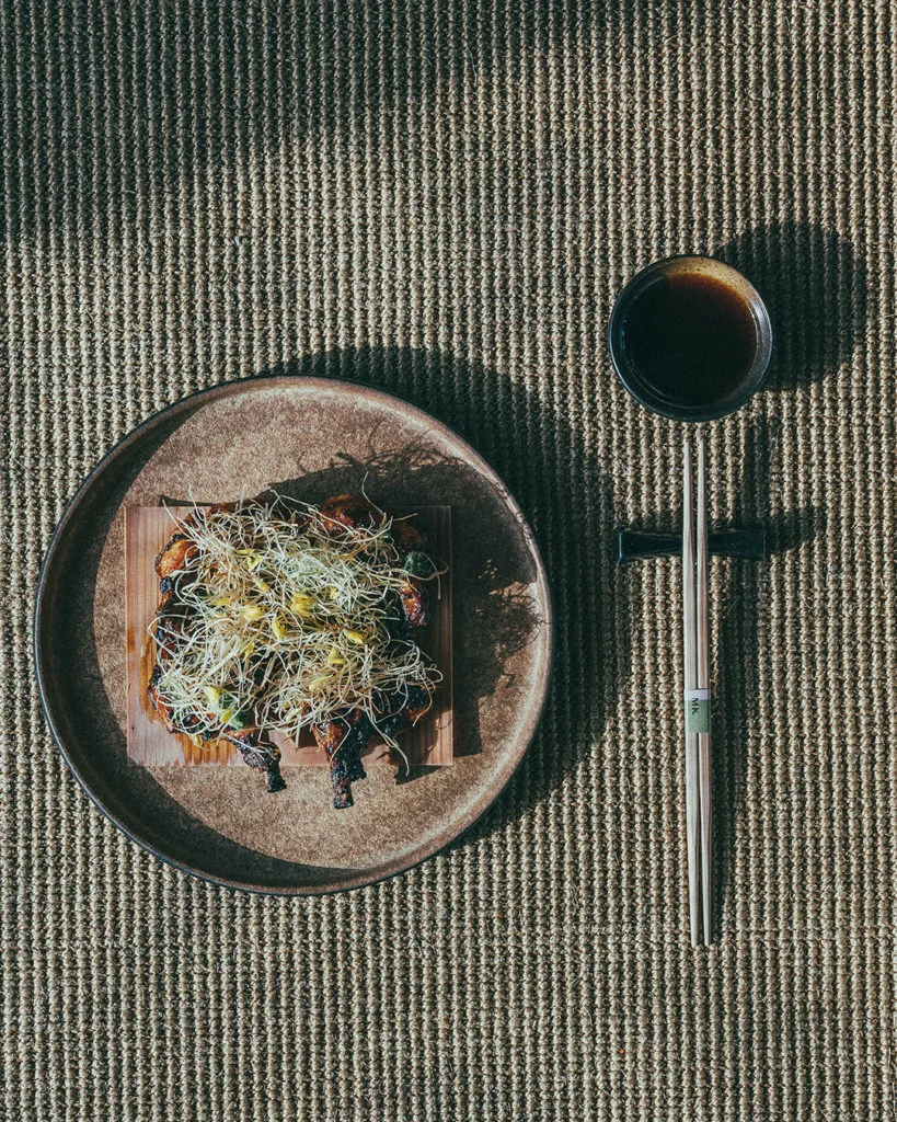 A plated dish and dipping sauce on a woven mat, seen from above