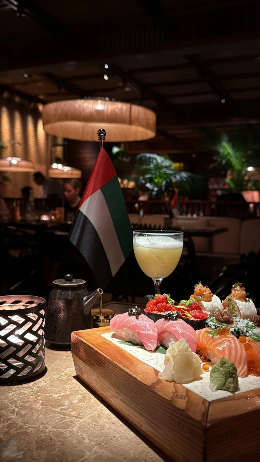 A sushi board with a cocktail and candle on a marble table