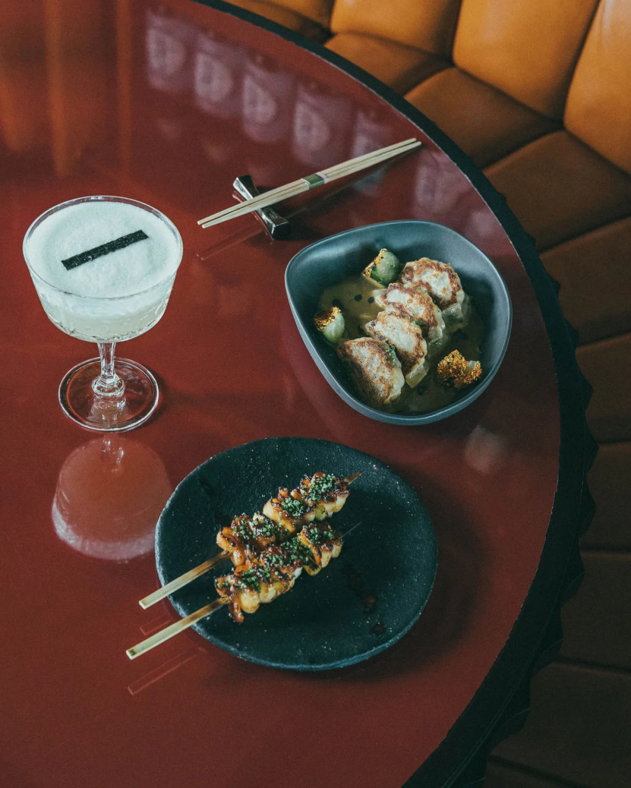 A shared spread of Japanese dishes and a cocktail on a lacquered table