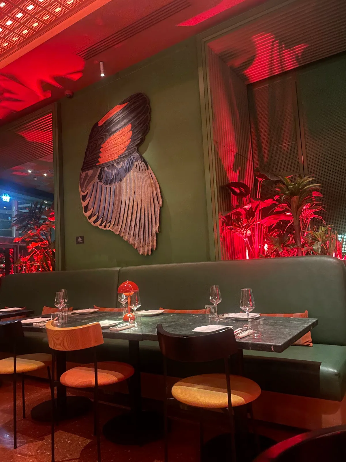 A banquette beneath bird-wing artwork lit in warm red light