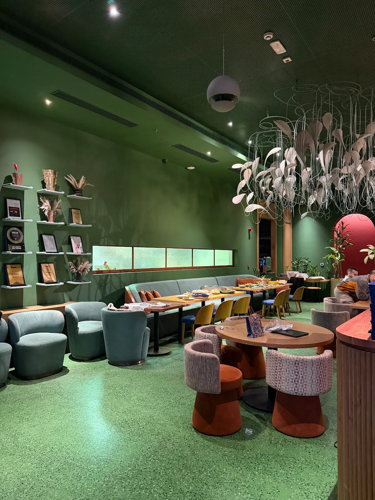 Green terrazzo lounge with curved velvet chairs and a feathered chandelier