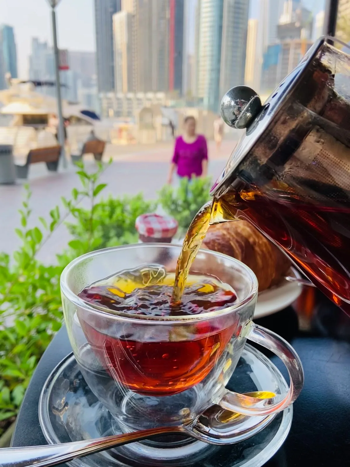 A pot of tea poured into a glass cup with the Dubai Marina skyline in the background