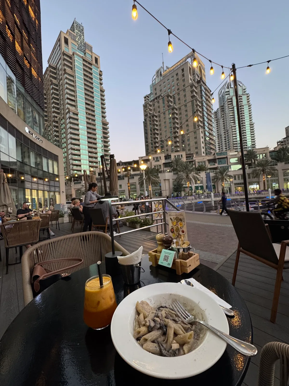 Marina Gate terrace at dusk with the Dubai Marina skyline and string lights