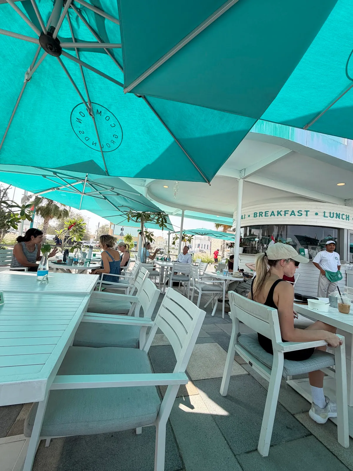 Guests seated at white tables under turquoise Common Grounds umbrellas on a sunny day