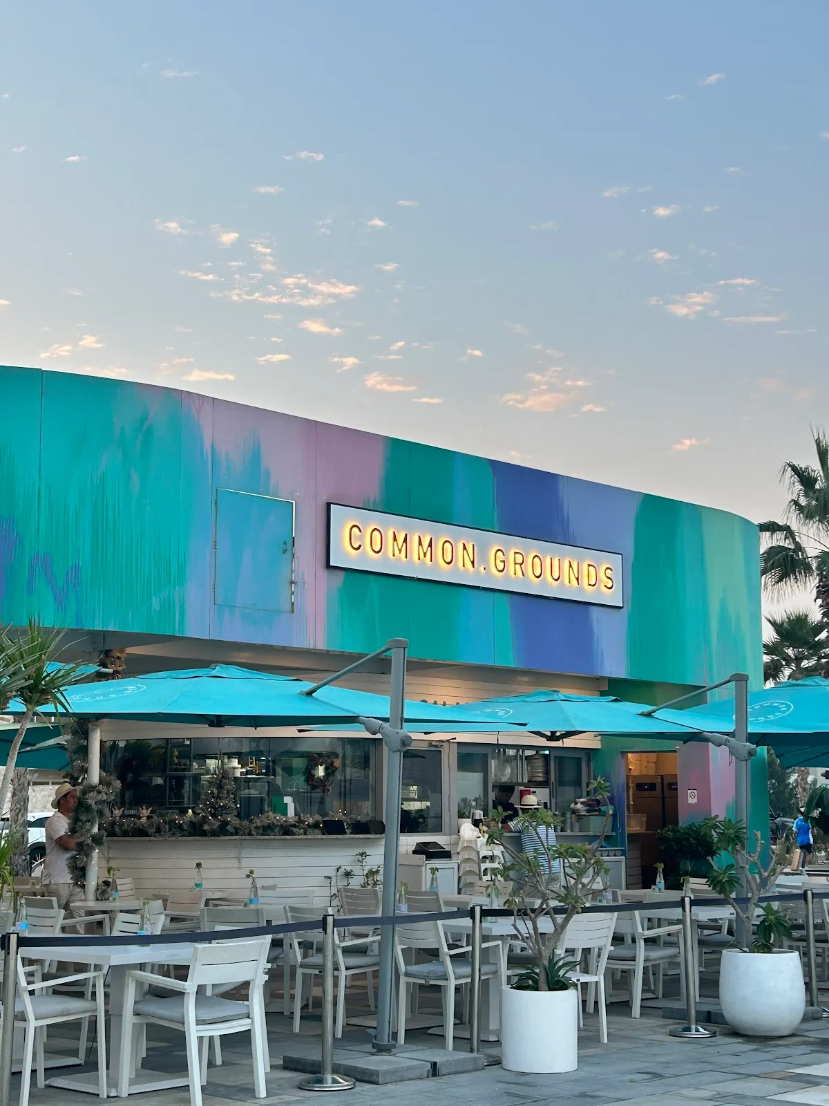 Common Grounds kiosk at dusk with turquoise umbrellas and a lit sign