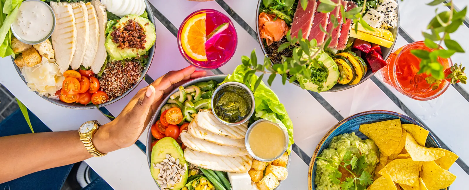 Several colourful salad and grain bowls with fresh drinks on a striped table