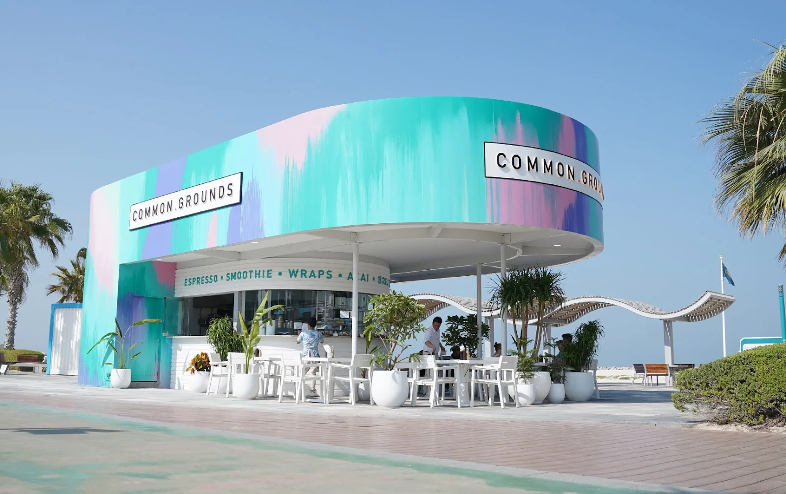 The colourful Common Grounds kiosk on the Kite Beach promenade in Dubai, with white outdoor seating under the sun