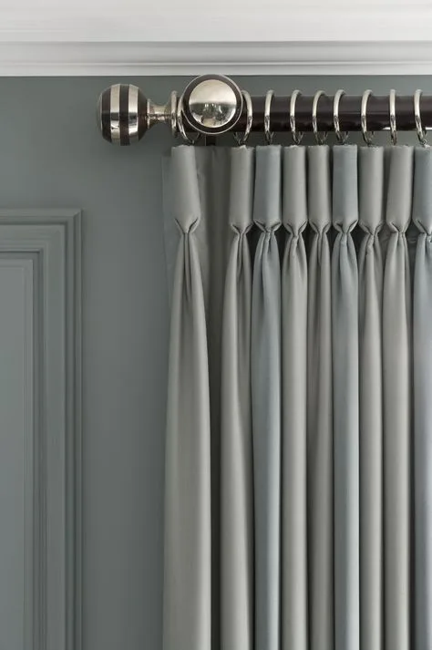Grey pinch-pleat curtain heading on a chrome pole