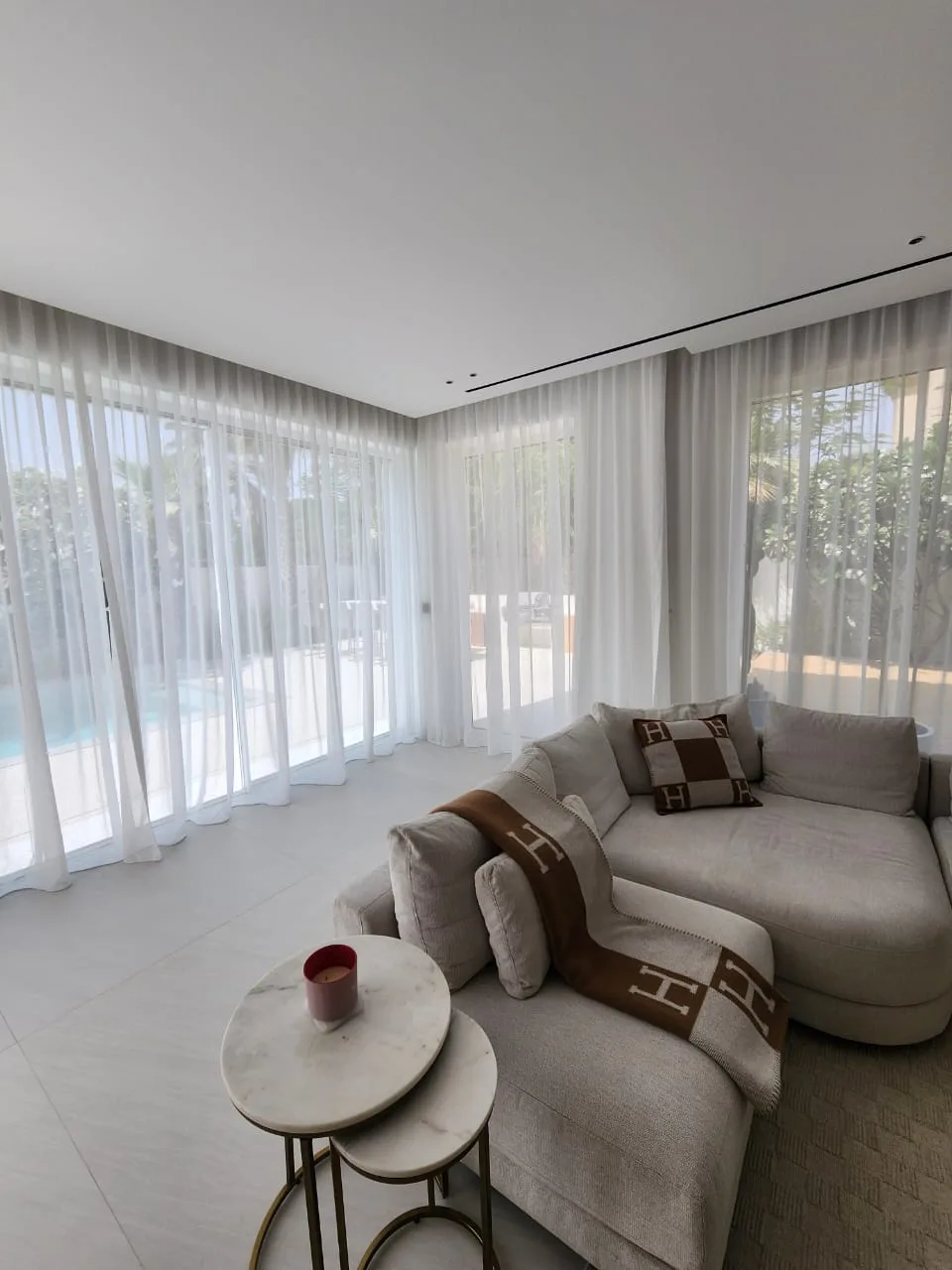 Floor-to-ceiling sheer curtains framing a bright Dubai living room with pool view