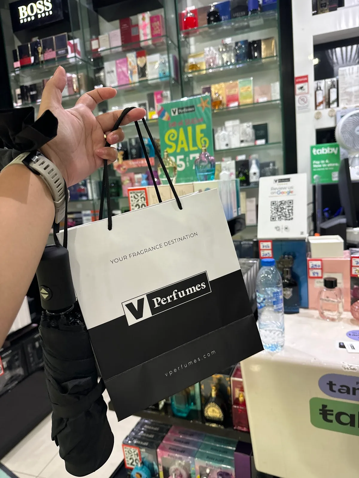A V Perfumes shopping bag held up inside the store, shelves of fragrances behind
