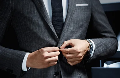 Close-up of a hand fastening a tailored grey pinstripe jacket