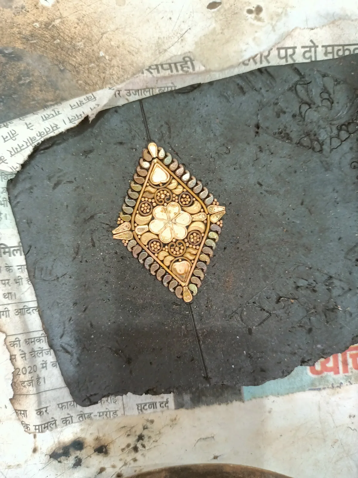 A detailed handmade gold pendant resting on a goldsmith's work surface