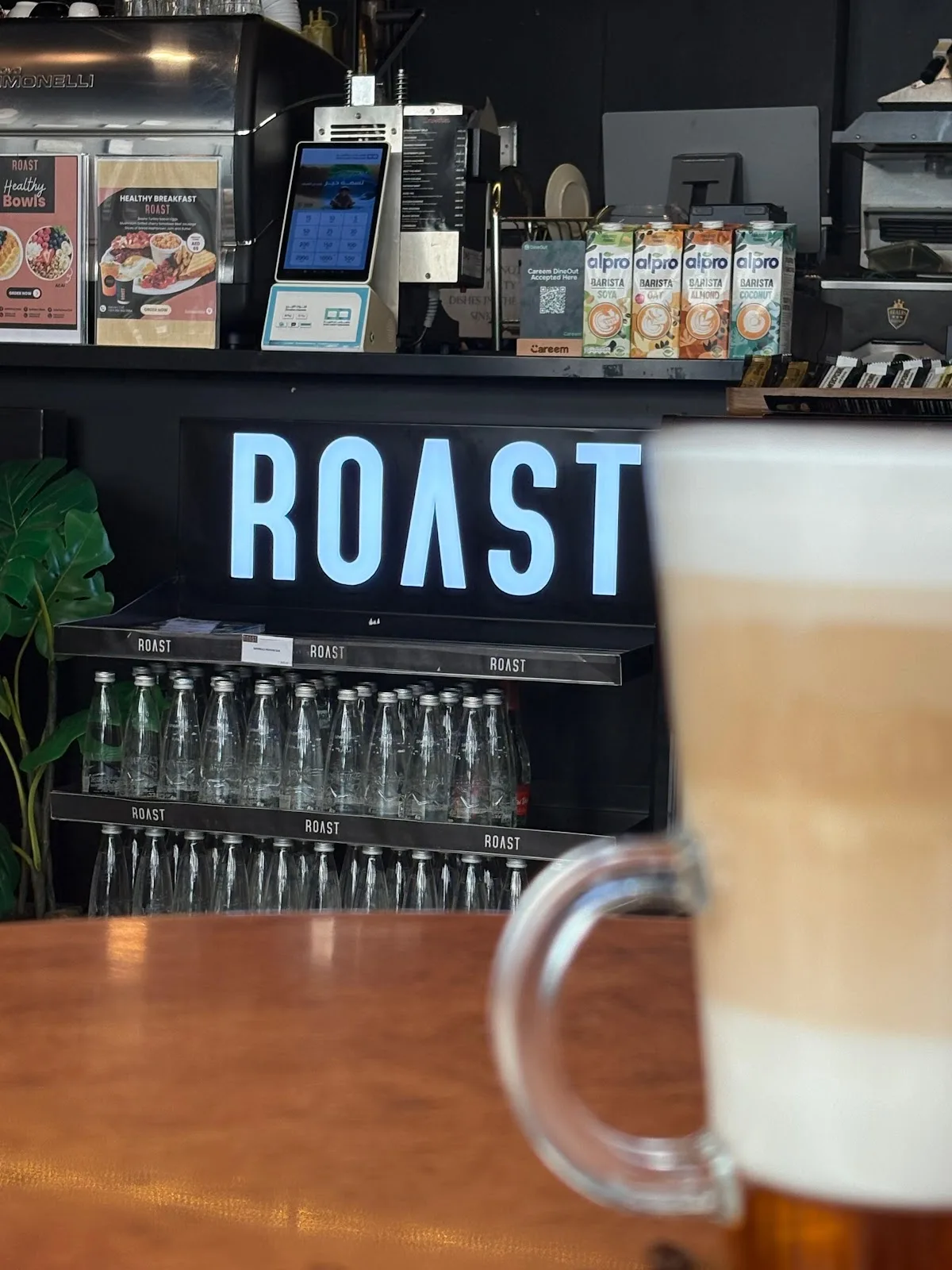 The illuminated ROAST sign behind the café counter with a latte in front