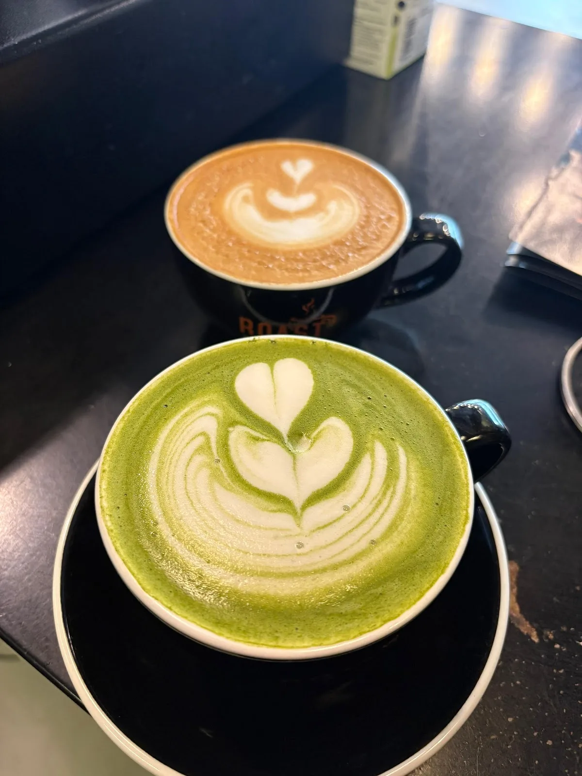 A matcha latte and a coffee latte with heart art, side by side
