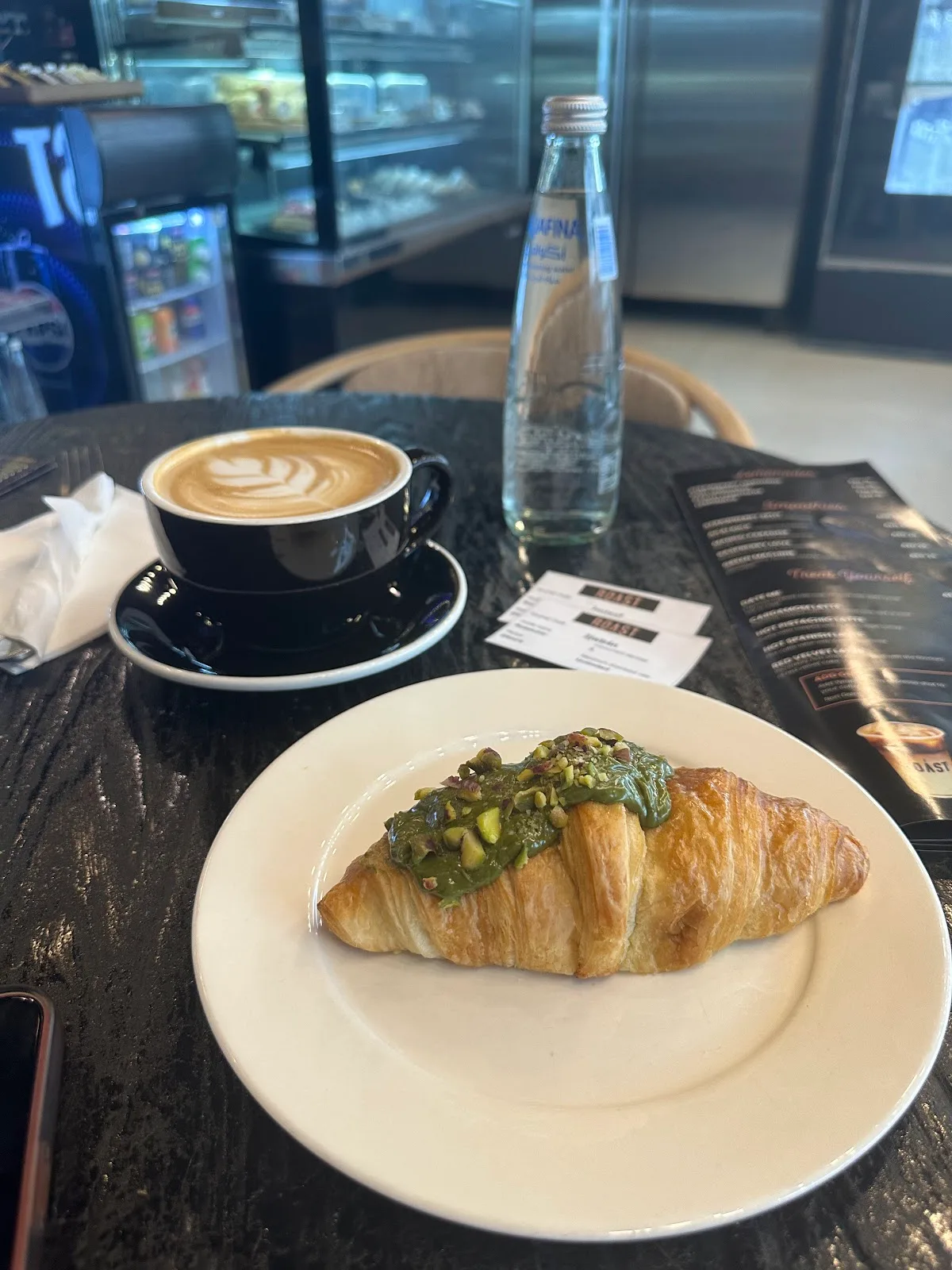 A pistachio-topped croissant with a latte and menu