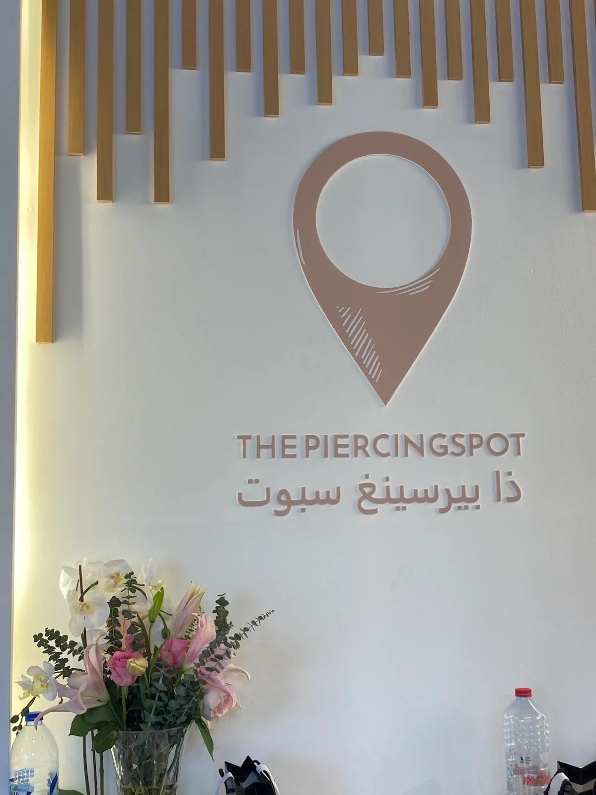 The Piercing Spot location-pin logo on the studio wall with fresh flowers