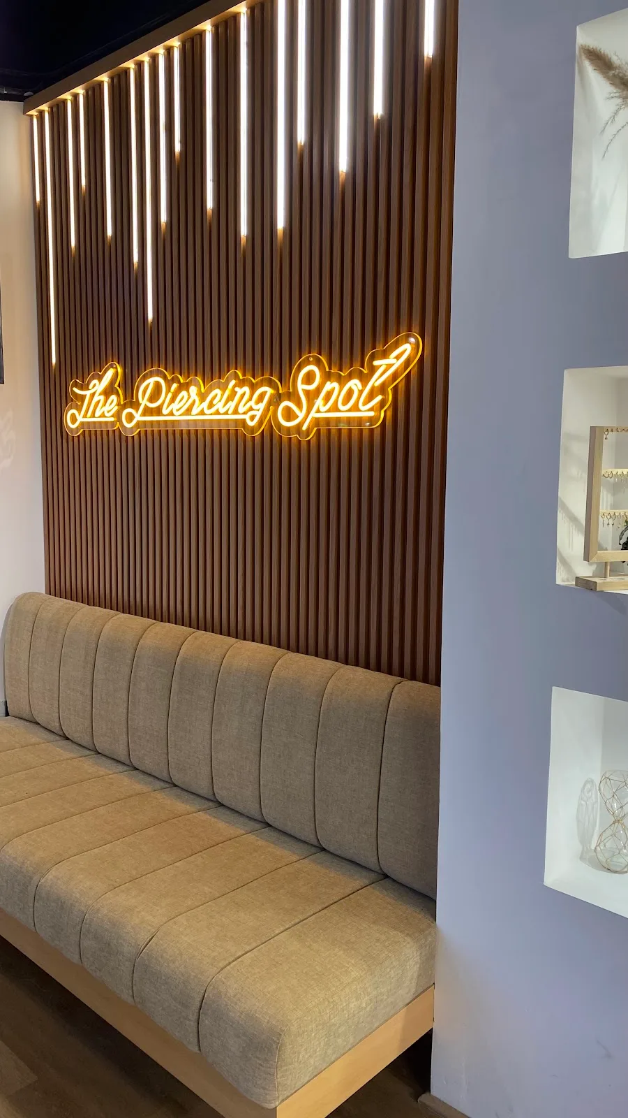 'The Piercing Spot' neon sign on a warm wood-slat wall above a bench