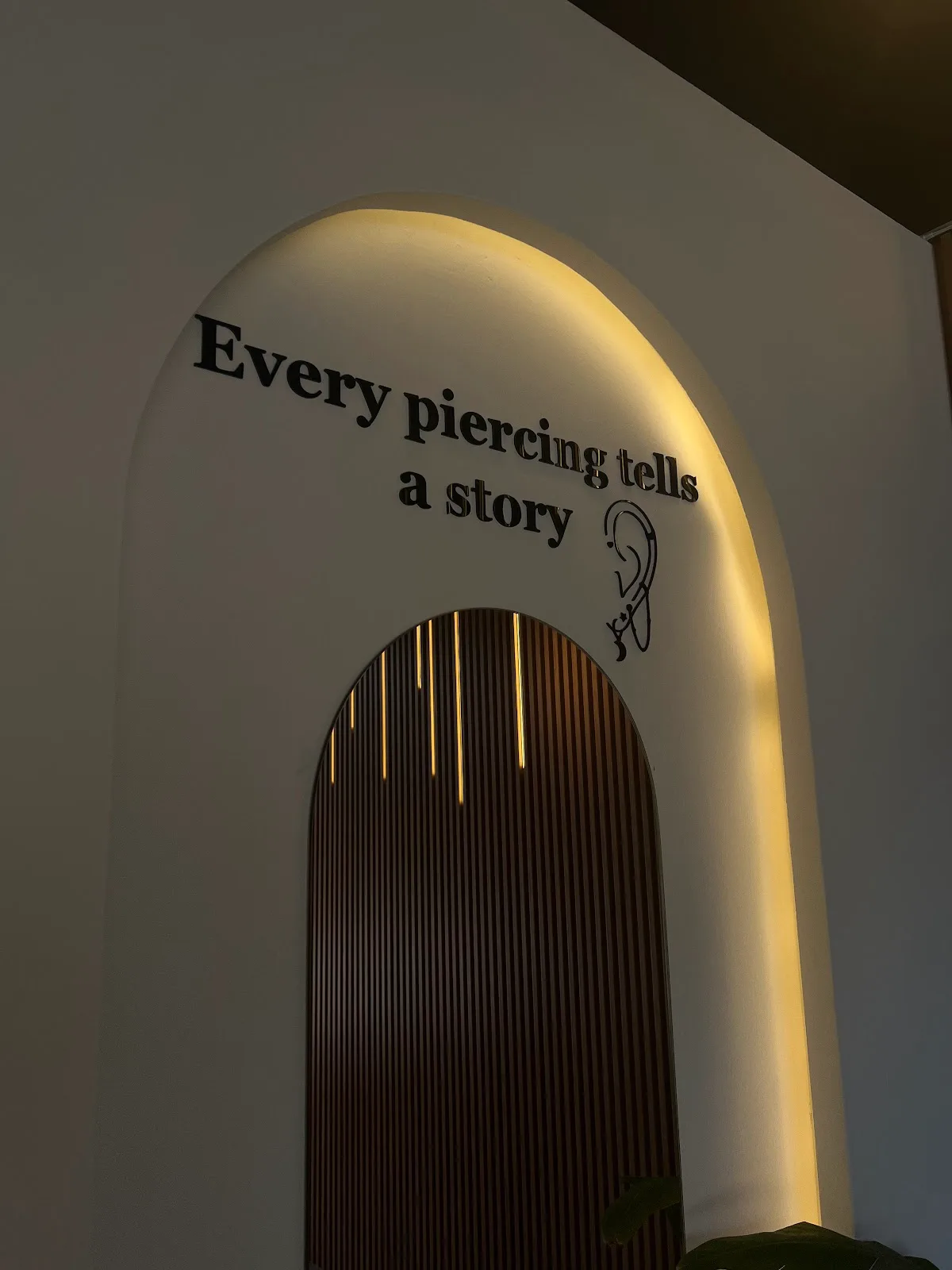 Studio wall reading 'Every piercing tells a story' beneath a softly lit arch
