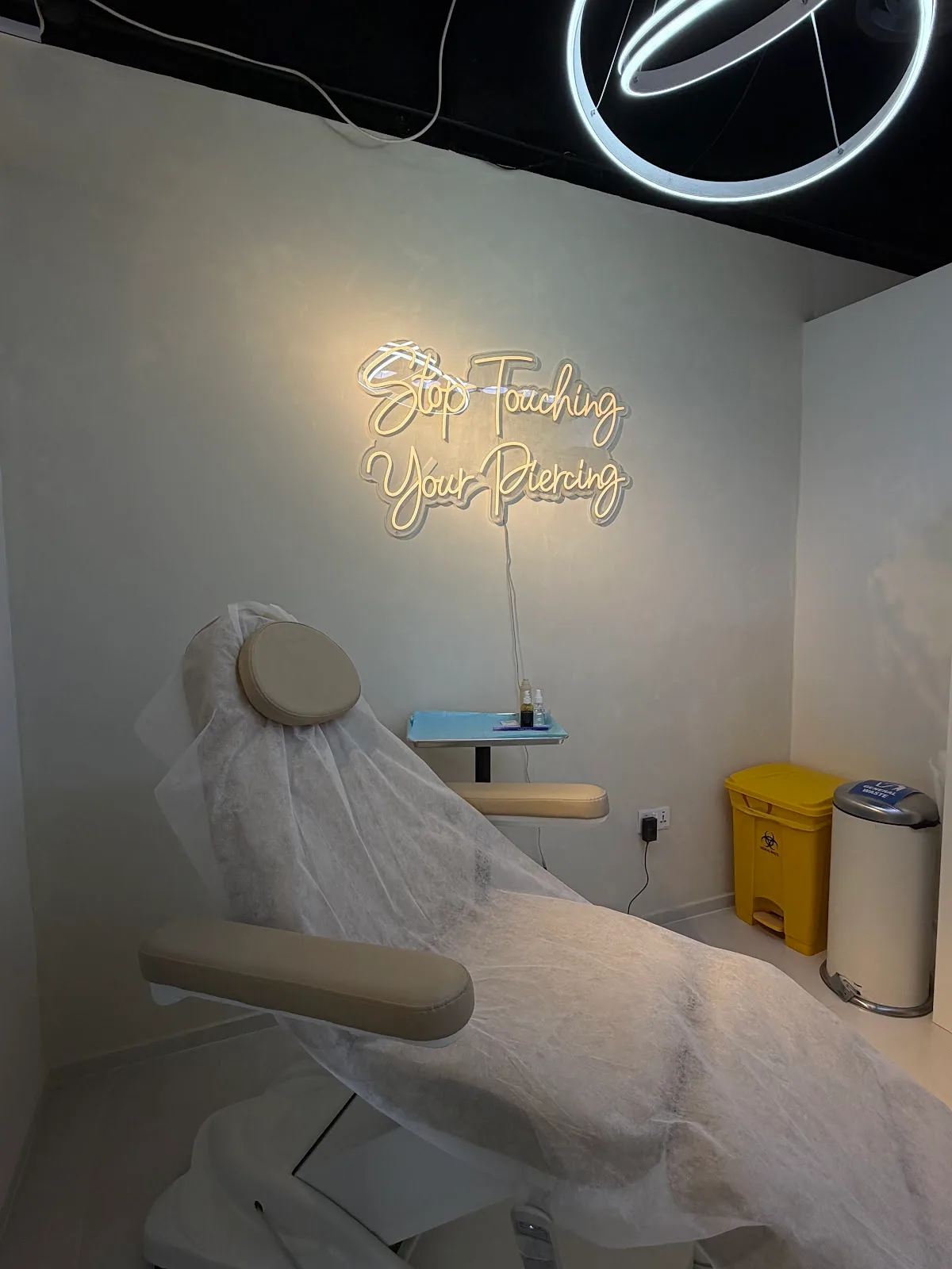 Piercing treatment room with a 'Stop touching your piercing' neon sign