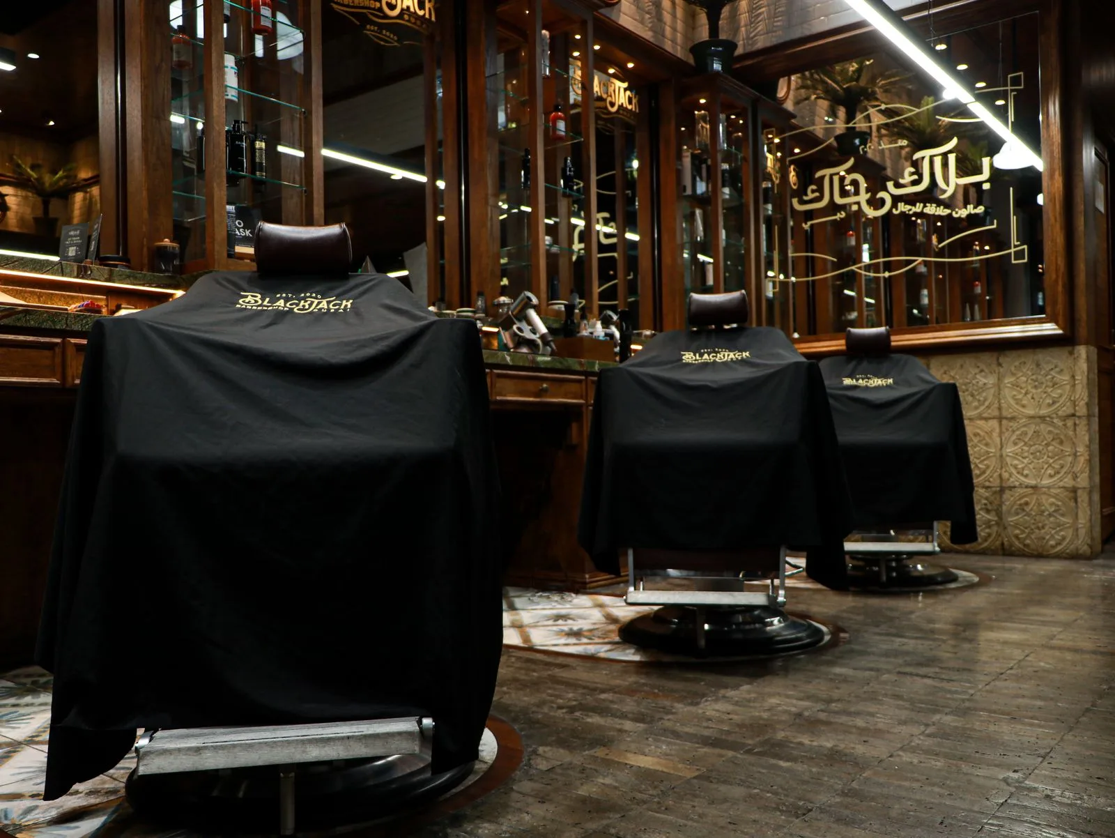 Row of barber chairs draped, with gold Arabic signage behind