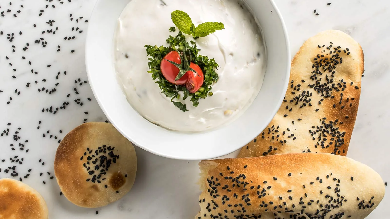 Creamy yogurt dip topped with herbs, served with fresh sesame flatbread
